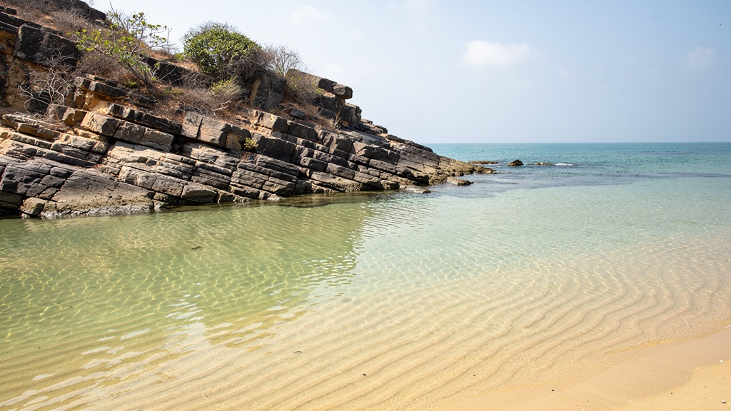 Shallow turquoise lagoon at Jallandhar beach with a rocky headland