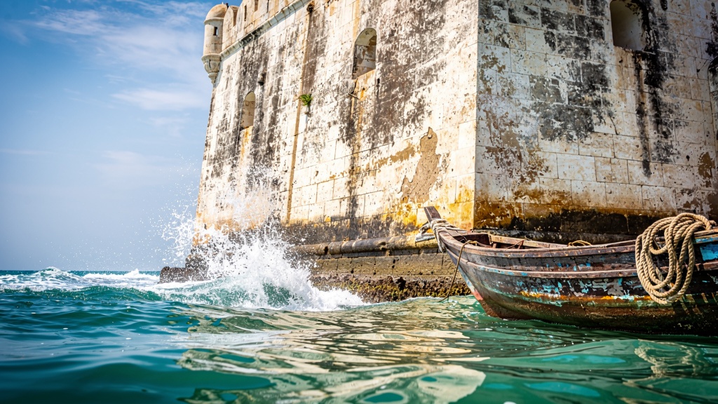 Weathered stone walls of Panikotha rising straight from the sea with waves at the base